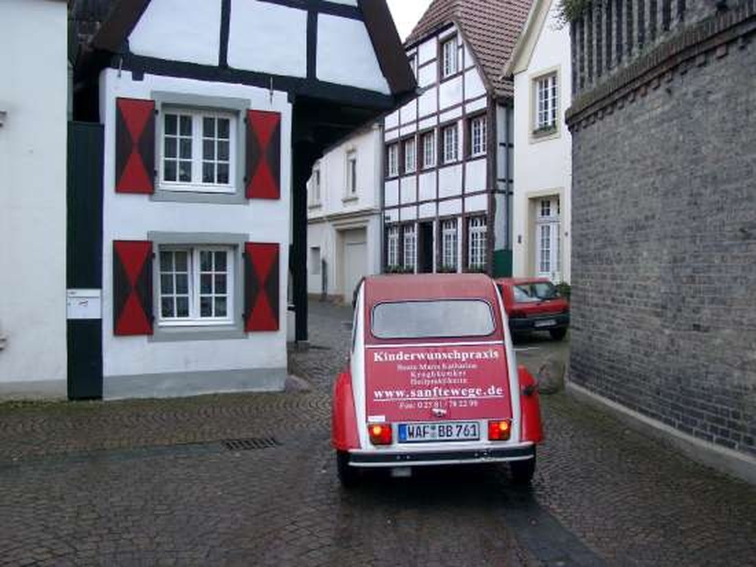 Roter Citroën 2CV mit der Aufschrift Kinderwunschpraxis und sanftewege.de in einer Altstadtgasse